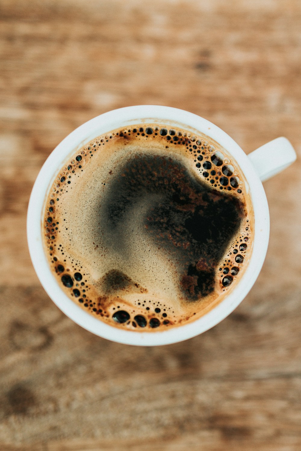 A white cup of black coffee on a wooden table